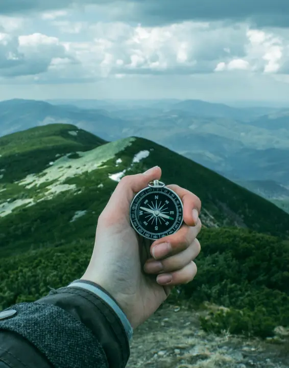 Person with compass, ready for adventure amid majestic mountain peaks.